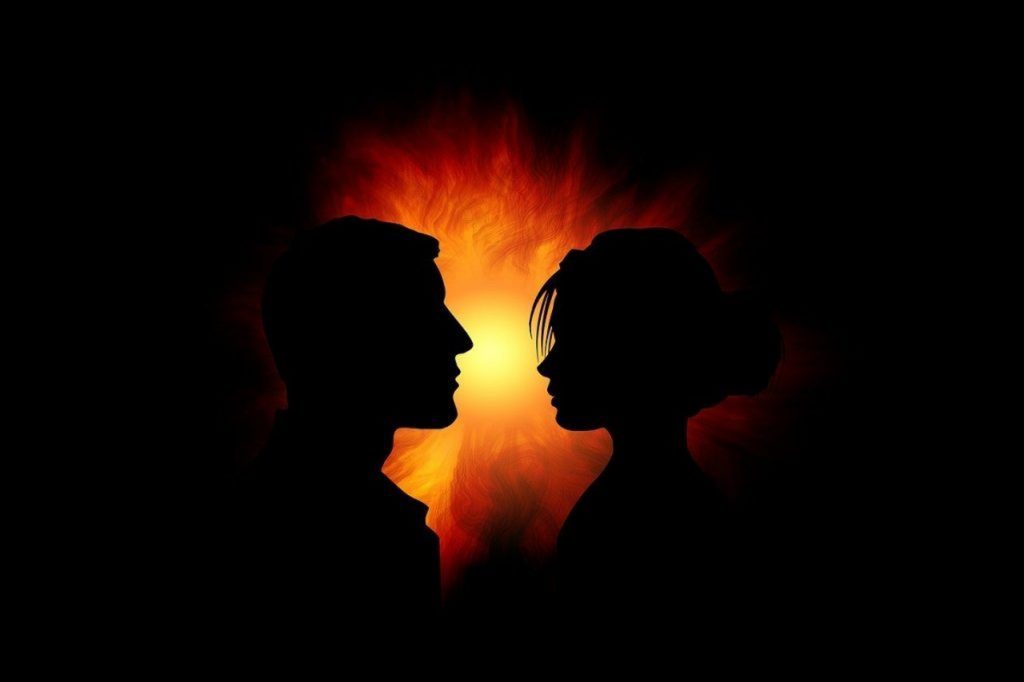 Silhouettes d’un homme et d’une femme se faisant face dans l’ombre, séparées par une lumière intense évoquant un conflit, une opposition ou un affrontement psychologique.