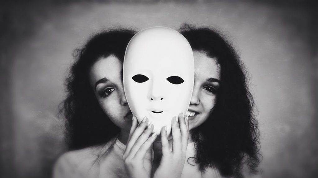 Portrait artistique en noir et blanc montrant une personne tenant un masque blanc devant son visage, suggérant une dualité entre apparence et identité.