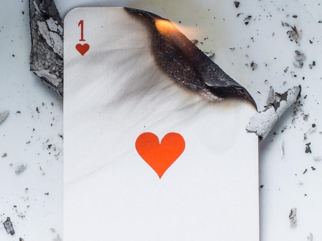 Carte à jouer représentant un cœur partiellement brûlé, entourée de cendres, symbolisant un refus amoureux et une rupture émotionnelle.