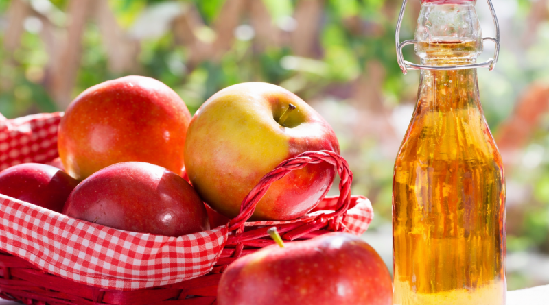Panier d’osier rempli de pommes rouges et jaunes posé à côté d’une bouteille de vinaigre doré, dans un décor lumineux et naturel.