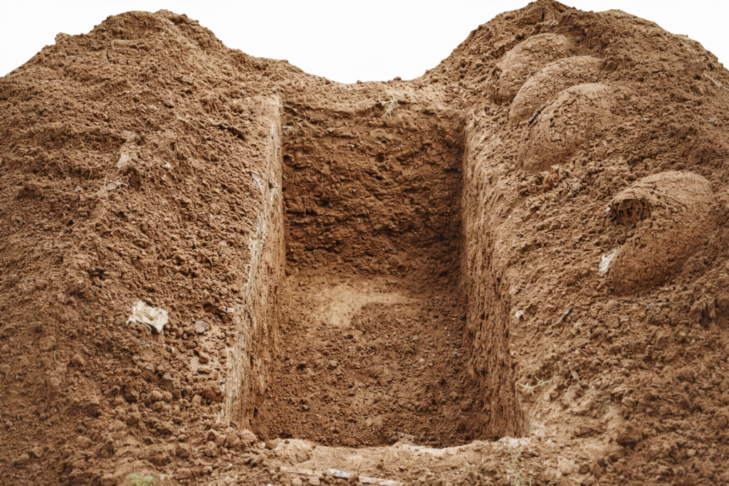 Tombe fraîchement creusée dans un sol de terre, symbolisant des funérailles simples et l’inhumation d’une personne sans ressources.