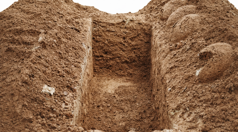 Tombe fraîchement creusée dans un sol de terre, symbolisant des funérailles simples et l’inhumation d’une personne sans ressources.