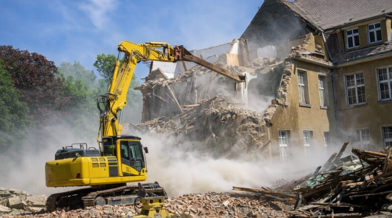 Maison en cours de démolition par une pelleteuse, nuage de poussière, gravats au sol, scène de destruction immobilière.