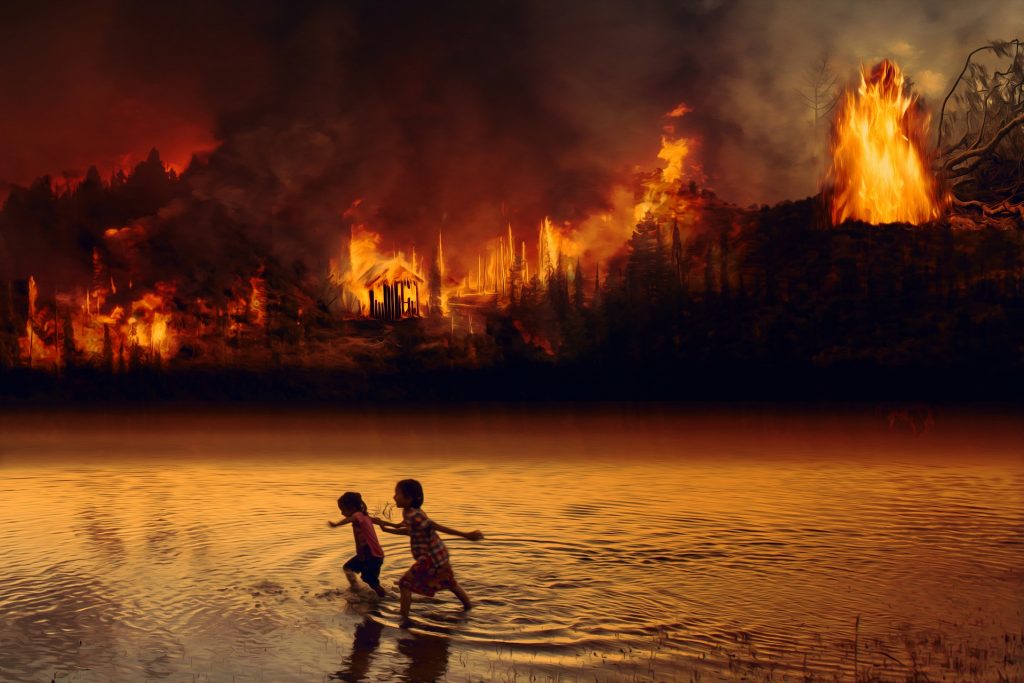 Deux enfants traversent une rivière peu profonde au premier plan tandis qu’une forêt en feu brûle intensément à l’arrière-plan, avec de hautes flammes et une épaisse fumée noire envahissant le ciel.