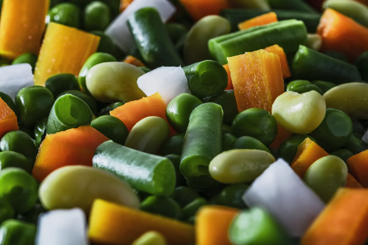 Mélange de légumes surgelés colorés avec carottes, haricots verts, pois et fèves, illustrant les aliments congelés avant préparation.