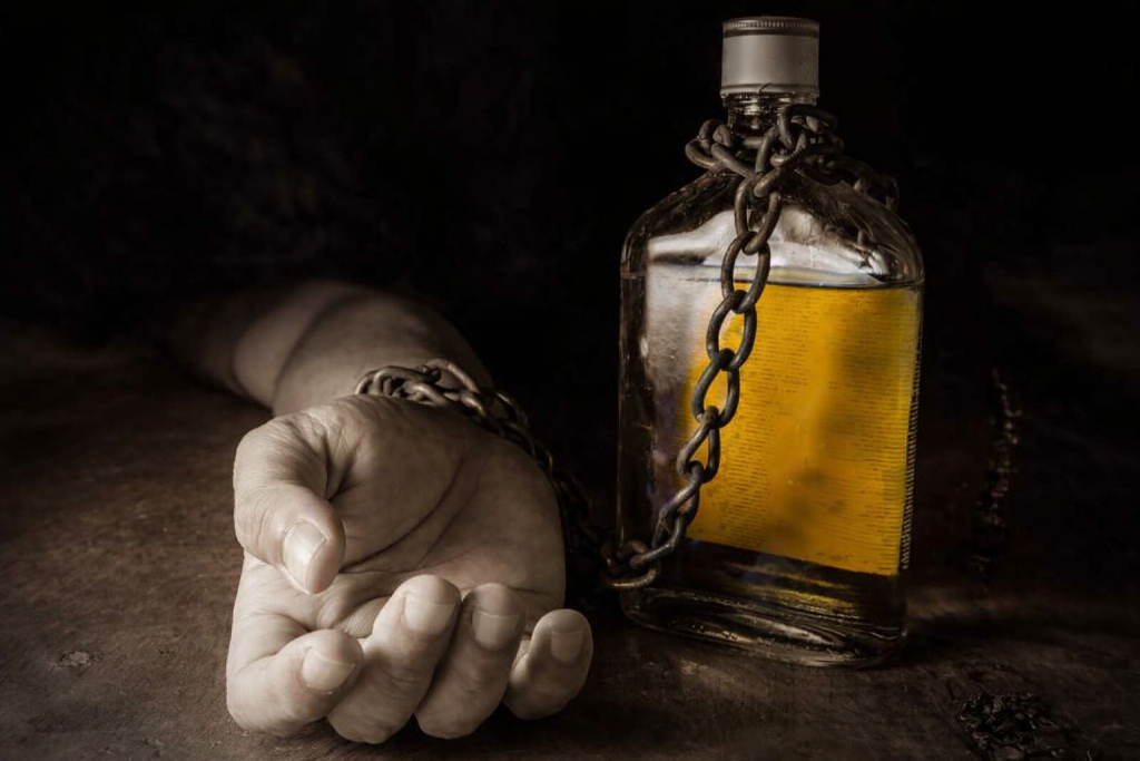 Main humaine entravée par une chaîne reliée à une bouteille d’alcool, symbolisant l’addiction et la perte de contrôle.
