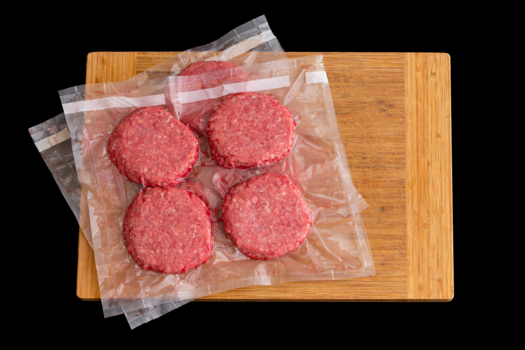 Steaks hachés crus emballés sous vide, disposés sur une planche en bois, illustrant la viande transformée avant cuisson.
