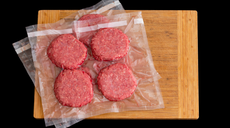 Steaks hachés crus emballés sous vide, disposés sur une planche en bois, illustrant la viande transformée avant cuisson.