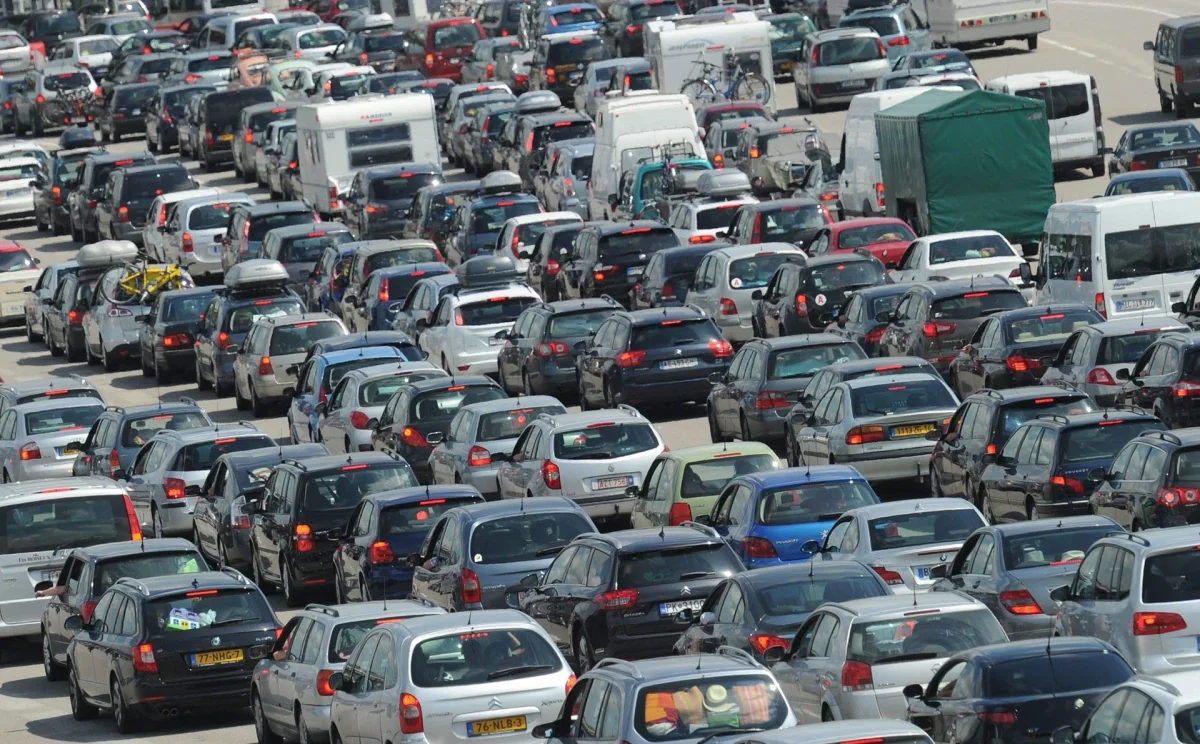 Embouteillage massif sur une autoroute, avec des centaines de voitures et de véhicules utilitaires immobilisés, pare-chocs contre pare-chocs, en pleine journée.