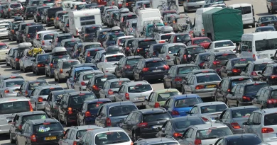 Embouteillage massif sur une autoroute, avec des centaines de voitures et de véhicules utilitaires immobilisés, pare-chocs contre pare-chocs, en pleine journée.