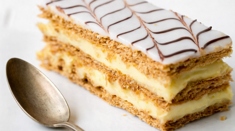 Part de mille-feuille traditionnel avec plusieurs couches de pâte feuilletée croustillante et de crème pâtissière, nappée d’un glaçage blanc décoré de lignes chocolatées.