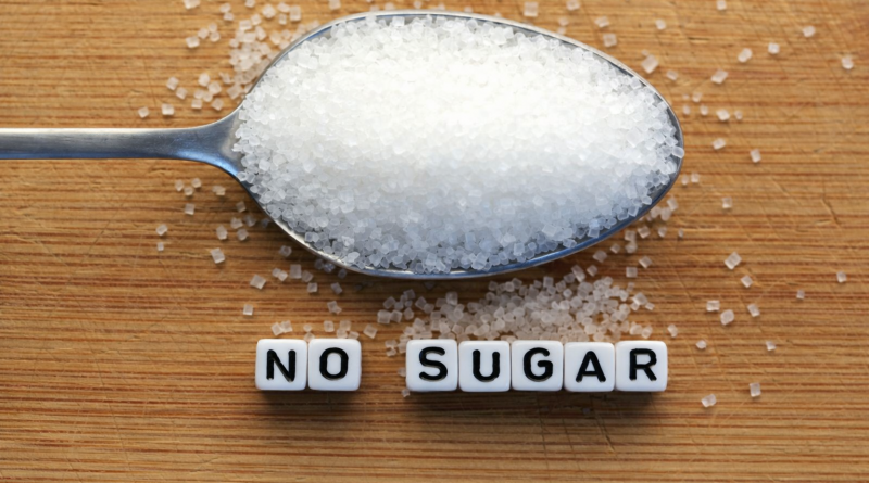 Cuillère remplie de cristaux blancs posée sur une surface en bois, avec l’inscription « no sugar » en lettres cubes, illustrant l’alimentation sans sucre.