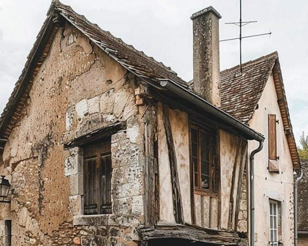 Maison médiévale à colombages avec encorbellement, murs en pierre et torchis, toiture ancienne et cheminée massive, architecture ancienne préservée