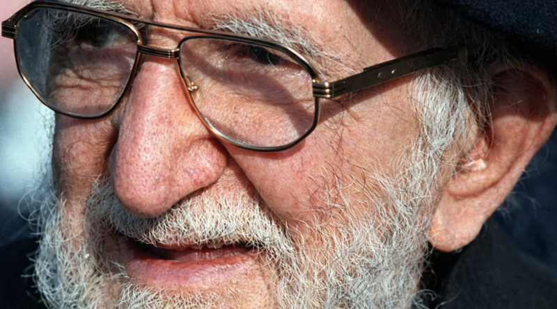 Portrait rapproché d’un homme âgé à la barbe blanche et aux lunettes, regard sérieux et bienveillant, éclairage naturel et arrière-plan flou.