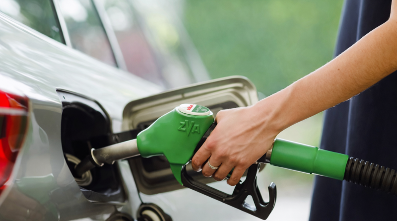 Main d’un conducteur tenant un pistolet de carburant vert pour faire le plein d’une voiture, illustrant un ravitaillement en carburant alternatif.