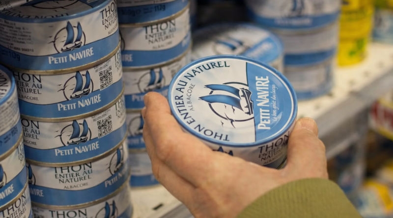 Main tenant une conserve de thon dans un rayon de supermarché, illustrant les inquiétudes liées à la présence de substances toxiques dans l’alimentation courante.