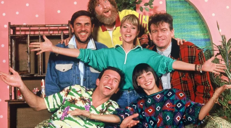 Groupe d’animateurs souriants posant ensemble sur un plateau de télévision coloré, décor rétro aux tons roses et verts, ambiance joyeuse et conviviale des années 1990.