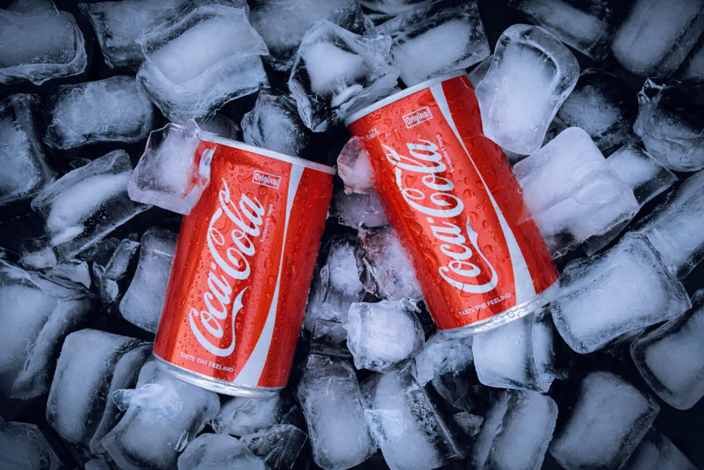 deux canettes de boisson gazeuse entourées de glaçons, illustrant une boisson rafraîchissante servie très froide