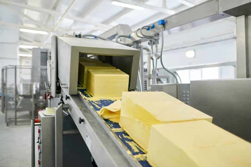 Blocs de beurre industriel sur une chaîne de production alimentaire, avançant sur un tapis roulant dans une usine moderne et lumineuse.
