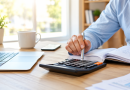 Personne utilisant une calculatrice devant un ordinateur portable et des documents administratifs pour vérifier ses comptes, illustration d'un trop-perçu CAF et des démarches de remboursement ou de contestation.