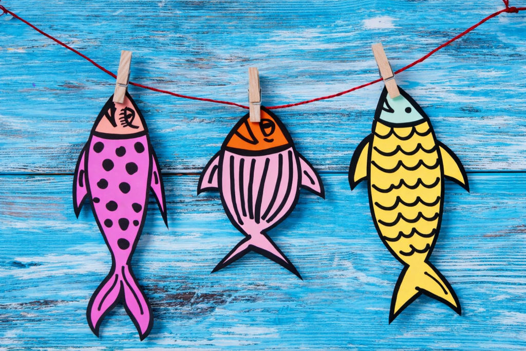poissons en papier colorés accrochés avec des pinces à linge sur un fil, évoquant la tradition du poisson d’avril