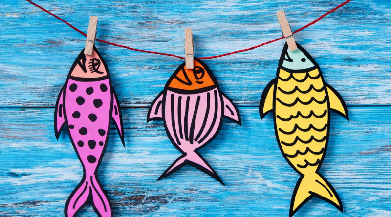 poissons en papier colorés accrochés avec des pinces à linge sur un fil, évoquant la tradition du poisson d’avril