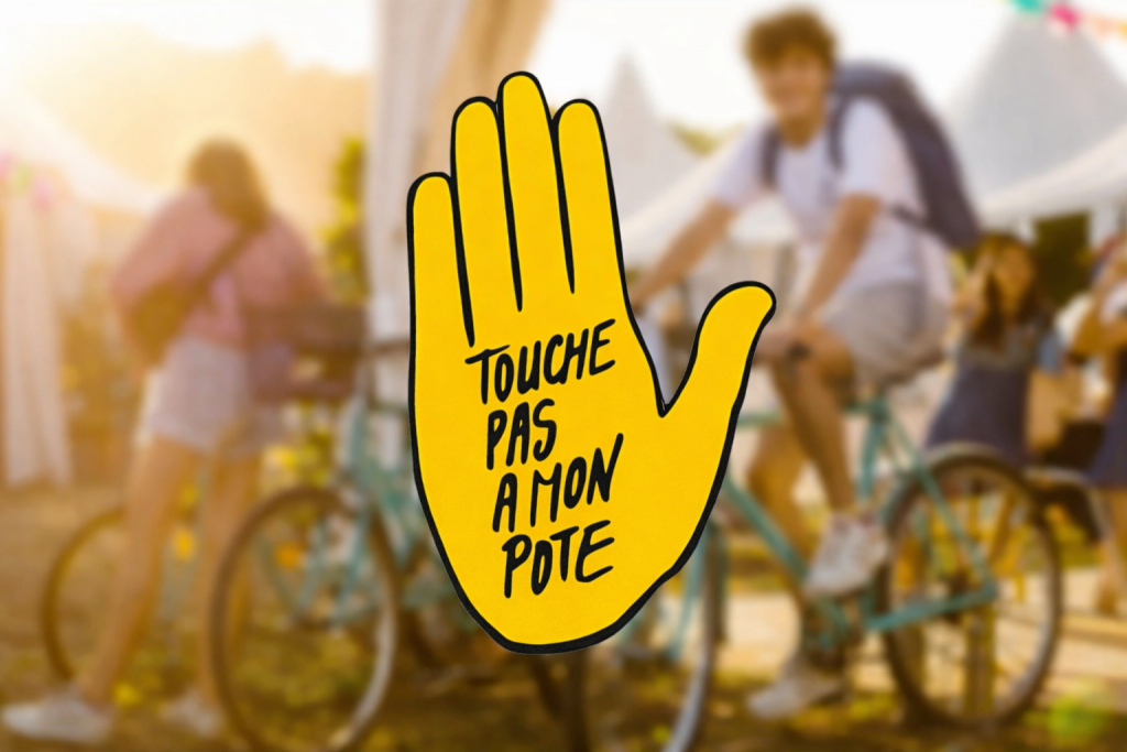Main jaune levée avec un message antiraciste inscrit, placée au premier plan devant une scène extérieure floue avec des personnes à vélo.