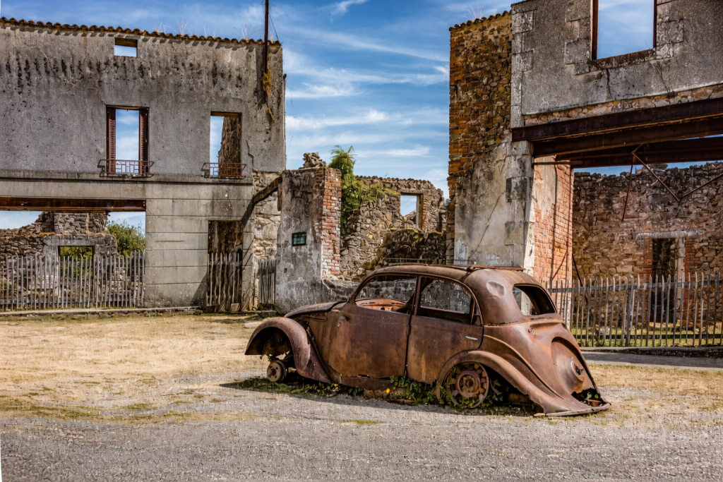 voiture ancienne rouillée abandonnée devant des maisons en ruines dans un village déserté