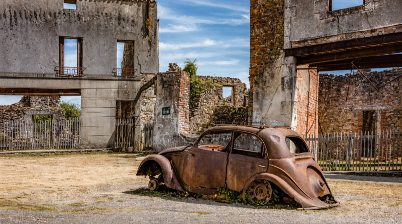 voiture ancienne rouillée abandonnée devant des maisons en ruines dans un village déserté