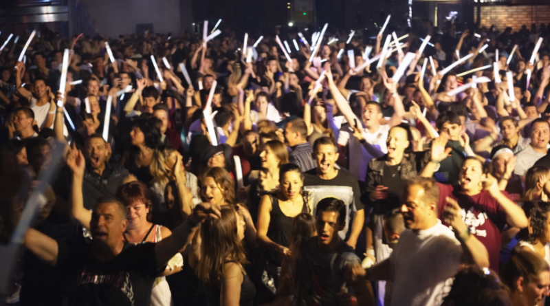 foule festive dansant lors d’une soirée populaire avec des bâtons lumineux levés