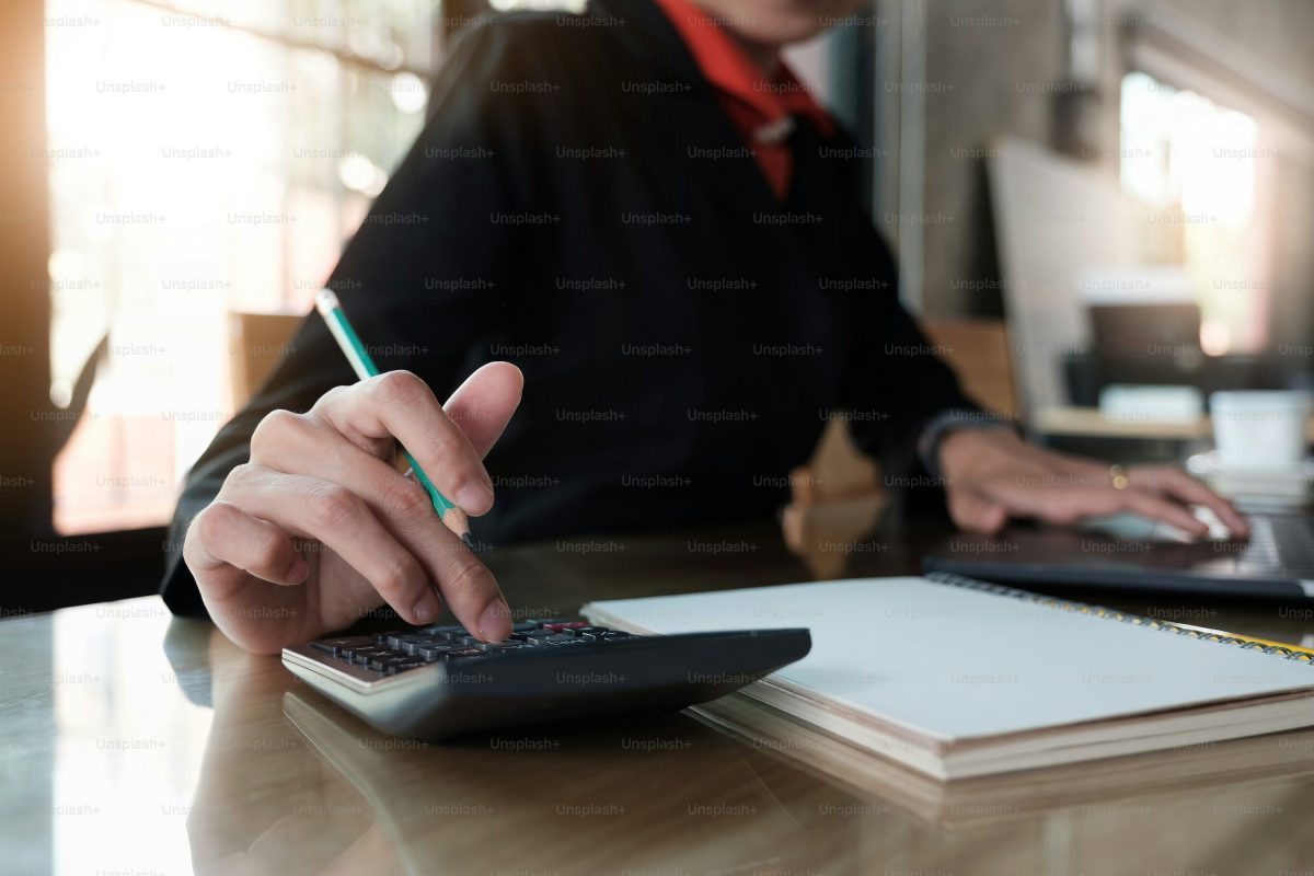 Personne assise à un bureau en train de vérifier des chiffres à l’aide d’une calculatrice, un stylo à la main, avec des documents administratifs posés devant elle, illustrant le contrôle d’un solde de fin de contrat avant signature.