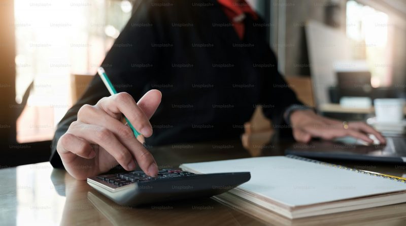 Personne assise à un bureau en train de vérifier des chiffres à l’aide d’une calculatrice, un stylo à la main, avec des documents administratifs posés devant elle, illustrant le contrôle d’un solde de fin de contrat avant signature.
