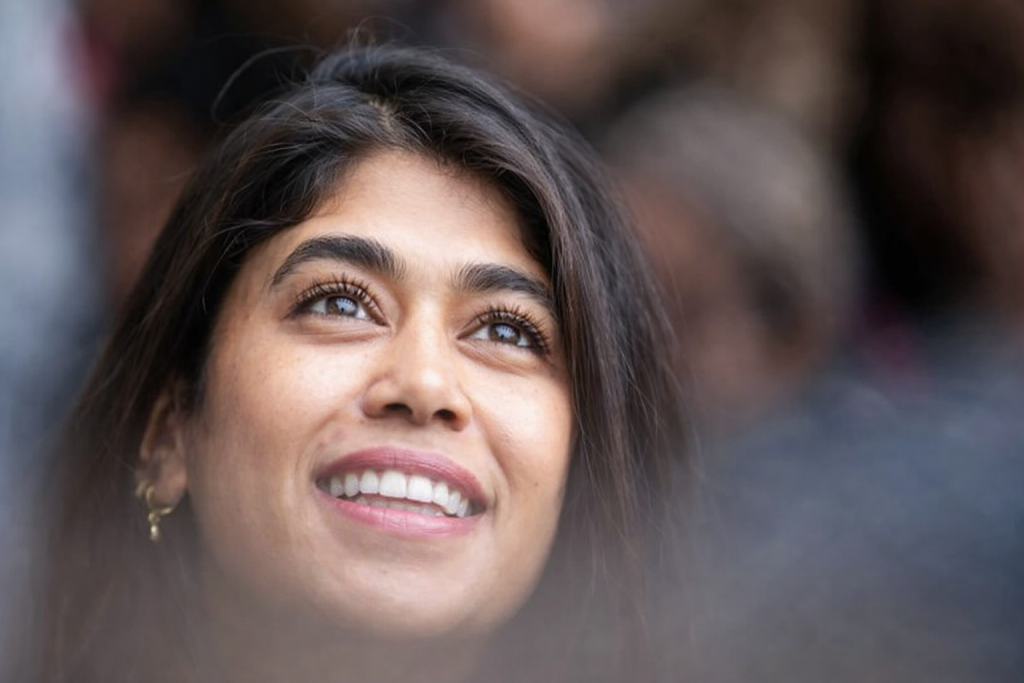 Portrait rapproché d’une femme souriante regardant vers le haut, avec un arrière-plan flou et une lumière naturelle douce mettant en valeur son visage.