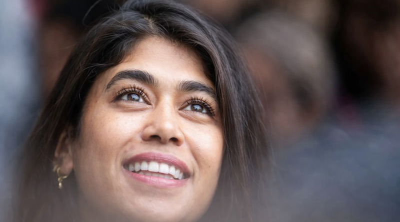 Portrait rapproché d’une femme souriante regardant vers le haut, avec un arrière-plan flou et une lumière naturelle douce mettant en valeur son visage.