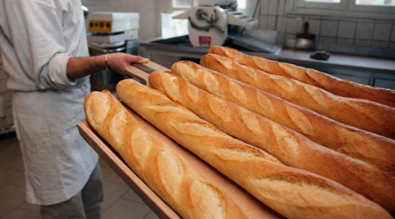 Baguettes de pain dorées et croustillantes alignées sur une pelle en bois, tout juste sorties du four dans une boulangerie artisanale.