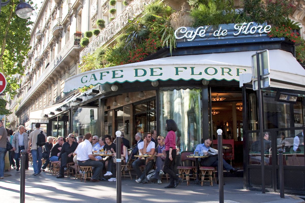 Terrasse de restaurant très fréquentée en centre-ville, avec des clients attablés à l’extérieur, une façade élégante et une ambiance touristique animée