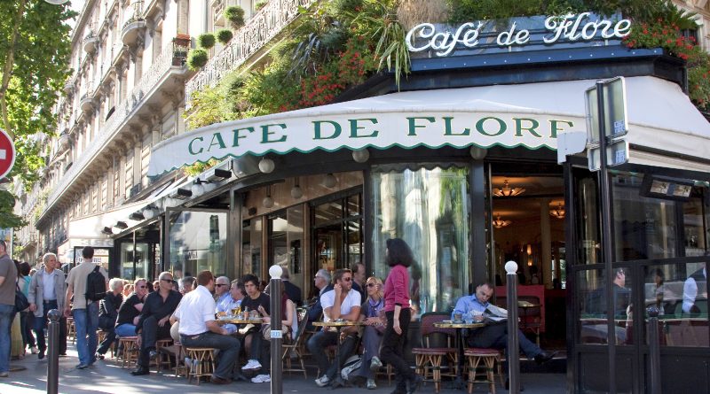 Terrasse de restaurant très fréquentée en centre-ville, avec des clients attablés à l’extérieur, une façade élégante et une ambiance touristique animée