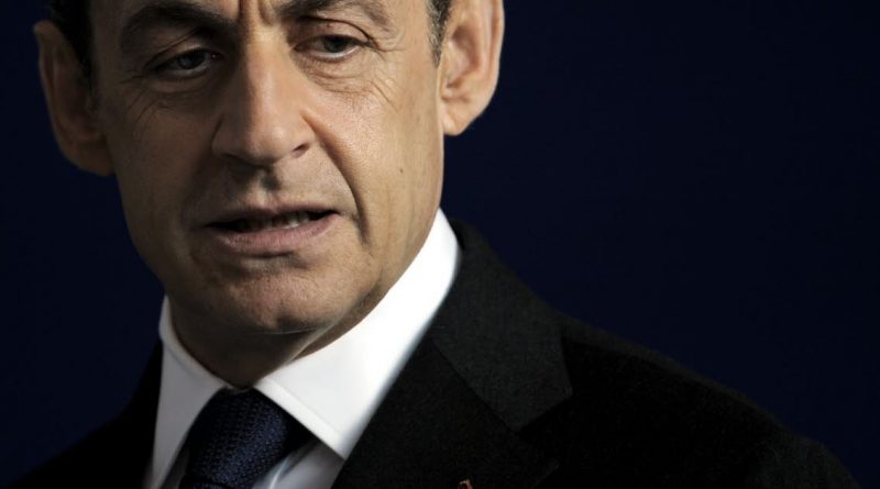 Homme politique mûr en costume sombre, visage sérieux et regard baissé, photographié sur fond sombre uni