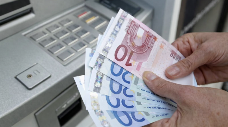 Mains tenant des billets en euros devant un distributeur automatique de billets