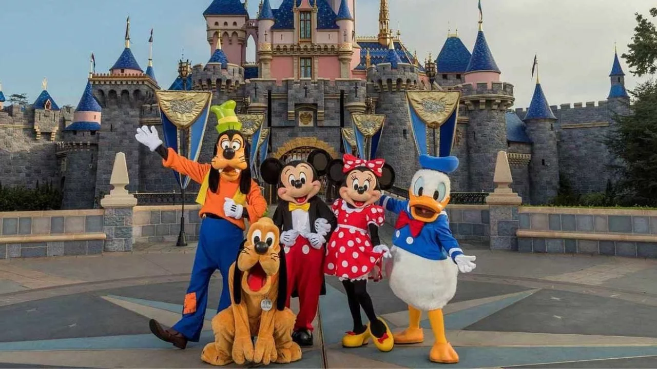Personnages emblématiques de Disney — Mickey, Minnie, Dingo, Pluto et Donald — posant devant le château du parc Disneyland, dans une scène colorée et festive.