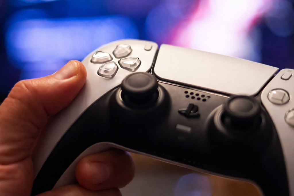 Main tenant une manette de jeu vidéo, gros plan sur les boutons et joysticks, fond lumineux flou en arrière-plan.