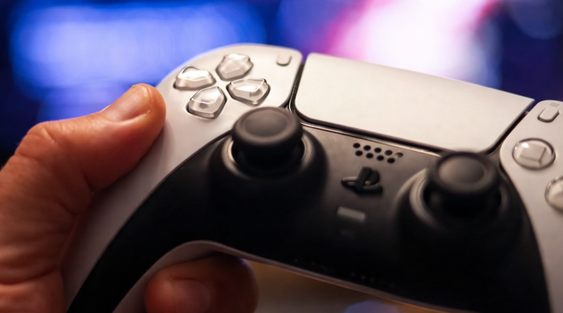 Main tenant une manette de jeu vidéo, gros plan sur les boutons et joysticks, fond lumineux flou en arrière-plan.