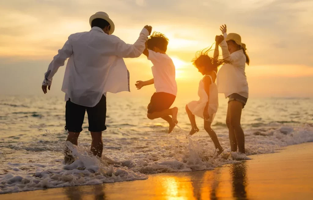 Famille de plusieurs générations sautant dans l’eau au bord de la mer au coucher du soleil, silhouettes joyeuses, vagues éclaboussantes, ambiance estivale et chaleureuse