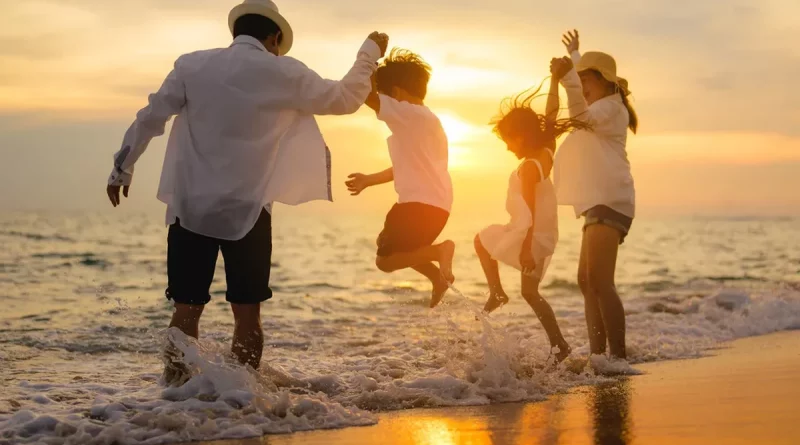 Famille de plusieurs générations sautant dans l’eau au bord de la mer au coucher du soleil, silhouettes joyeuses, vagues éclaboussantes, ambiance estivale et chaleureuse