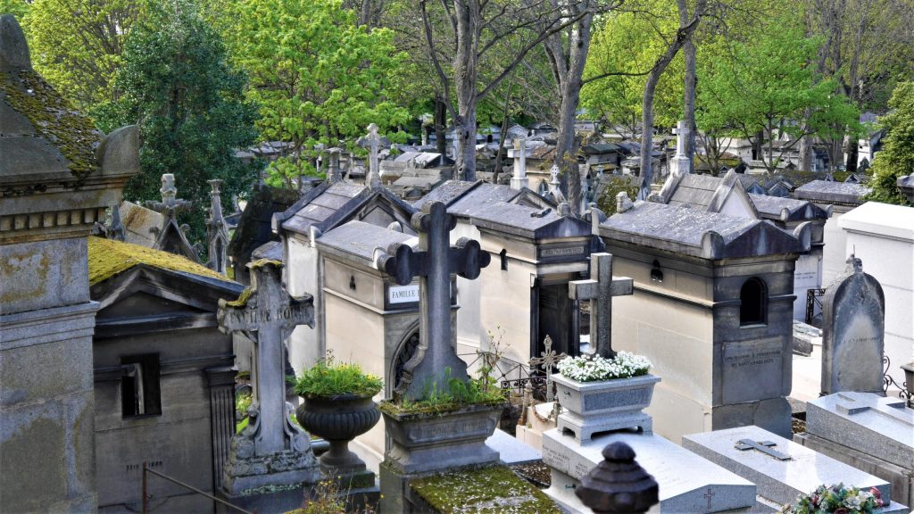 Allée de cimetière ancien avec tombes en pierre et croix funéraires entourées d’arbres verdoyants au printemps