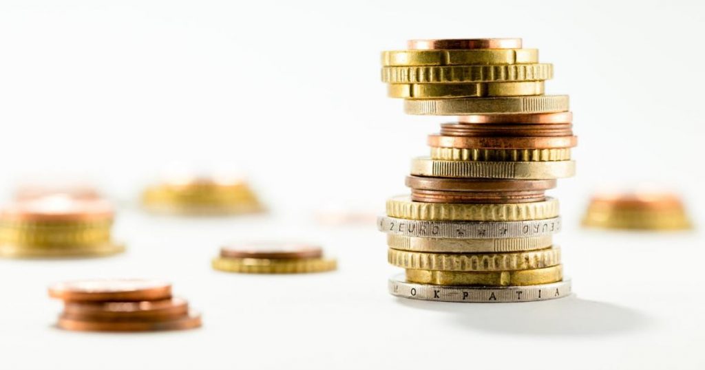 Pile de pièces de monnaie empilées de manière instable sur fond clair, symbolisant un déséquilibre financier