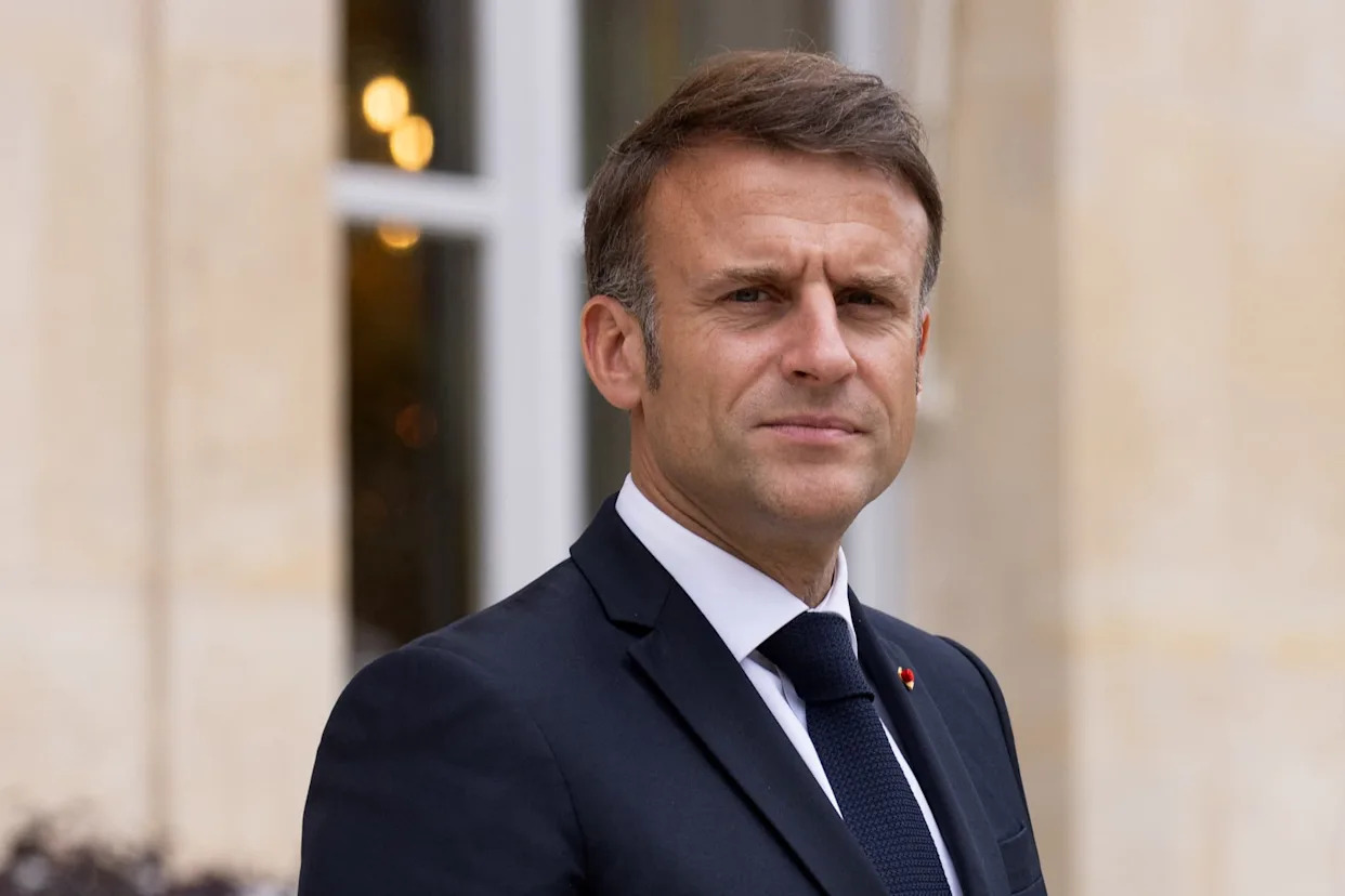 Portrait du président français debout en costume sombre devant une façade officielle, regard sérieux tourné vers l’objectif.