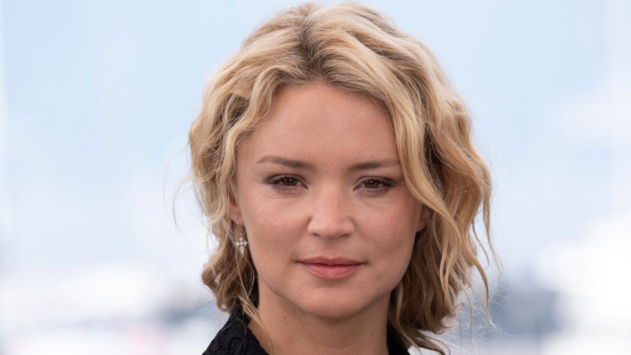 Portrait de Virginie Efira en extérieur, visage de face, expression sérieuse, cheveux blonds ondulés, sur un fond flou de ciel et de lumière naturelle.
