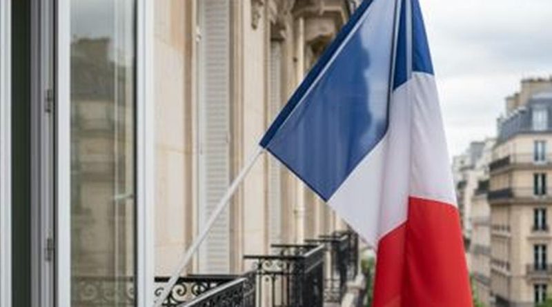 Fenêtre d’appartement ornée d’un drapeau tricolore français flottant au vent.