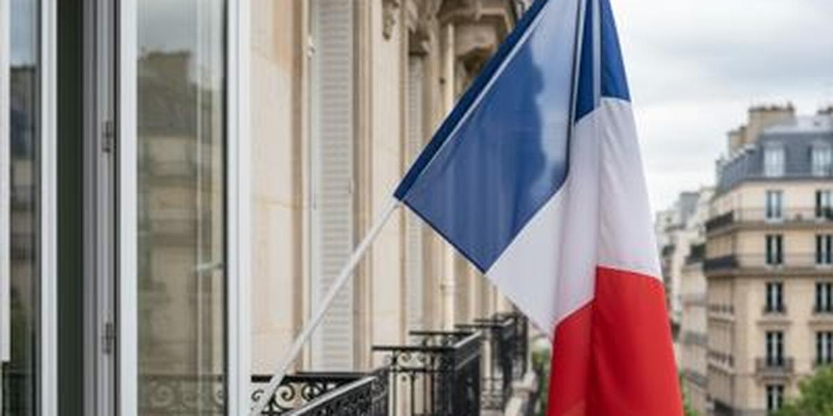 Fenêtre d’appartement ornée d’un drapeau tricolore français flottant au vent.